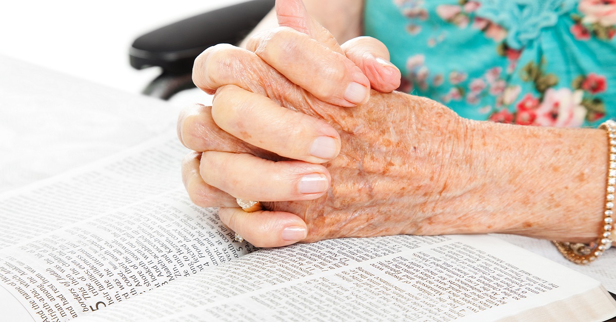 An elderly lady's hands interlaced and resting on her lap.